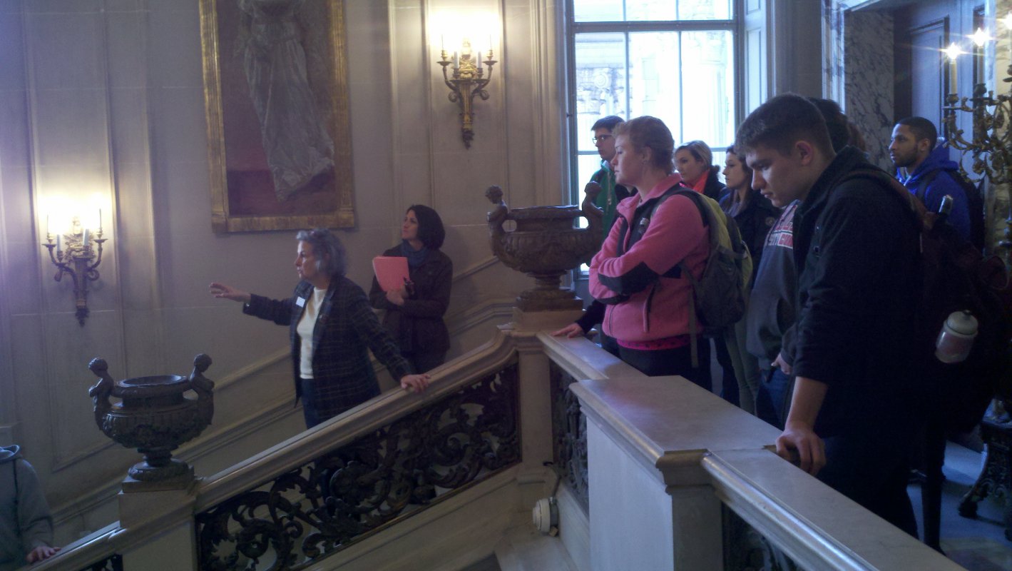 A tour guide at The Society of the Cincinnati explains to students and Dr. Mazzenga the significance of large paintings adorning the walls.